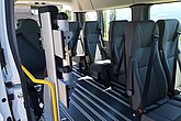 Eingangsbereich eines größeren Fahrzeugs mit Sitz- und Rollstuhlplätzen sowie einer Kopf- und Rückenstütze für Rollstuhlfahrer im vorderen Bereich.