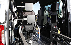 Eine Frau im Rollstuhl sitzt im hinteren Fahrzeugbereich und lehnt ihren Kopf an eine Kopf- und Rückenstütze.