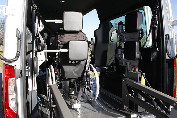 Eine Frau im Rollstuhl sitzt im hinteren Fahrzeugbereich und lehnt ihren Kopf an eine Kopf- und Rückenstütze.